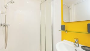 Um banheiro moderno com box de vidro, pia branca e uma parede de destaque amarela.