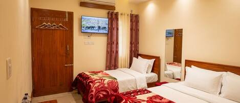 A hotel room with two beds, a television, an air conditioning unit, and a wooden door.