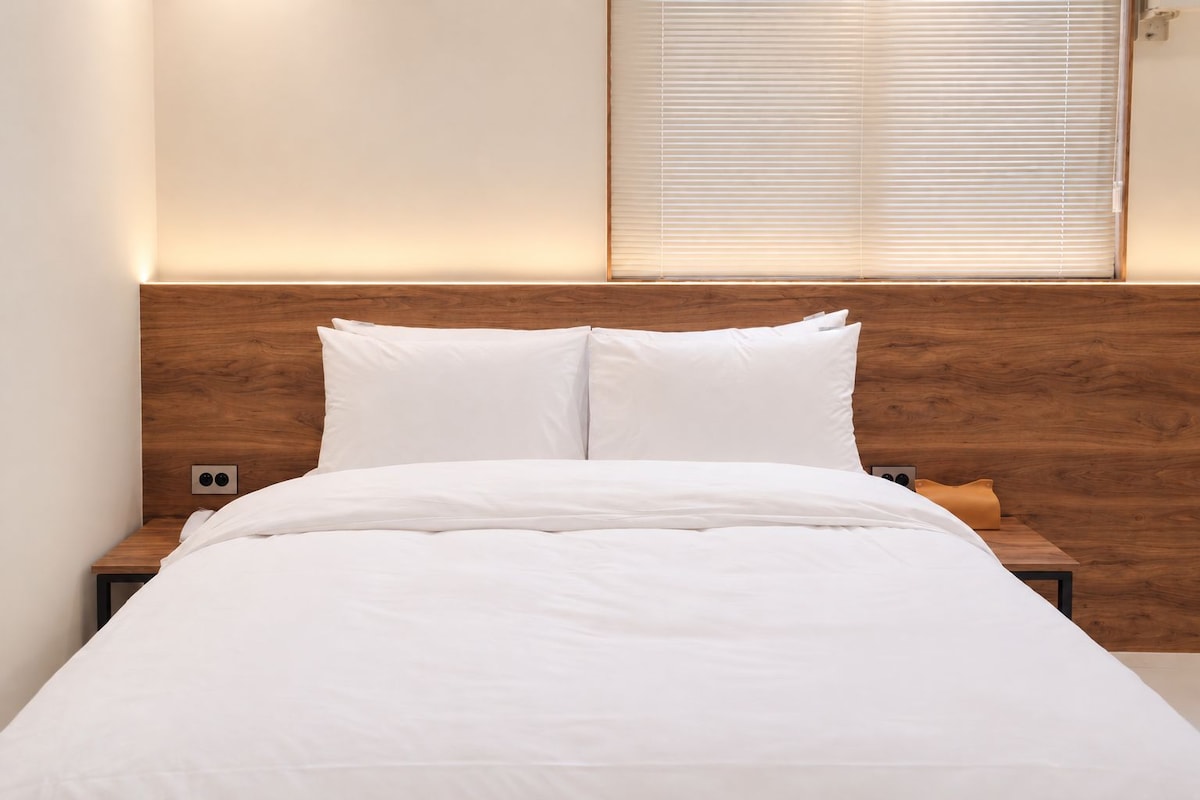 Ein ordentlich bezogenes Bett mit weißer Bettwäsche, ein Holz-Kopfteil und ein Nachttisch mit einer Lampe.