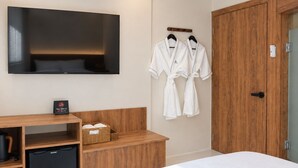 Une chambre d’hôtel avec un lit, un téléviseur fixé au mur, des meubles en bois et un porte-peignoir avec des peignoirs.