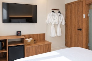 Ein Hotelzimmer mit einem Bett, einem an der Wand montierten Fernseher, Holzmöbeln und einem Bademantelständer mit Bademänteln.