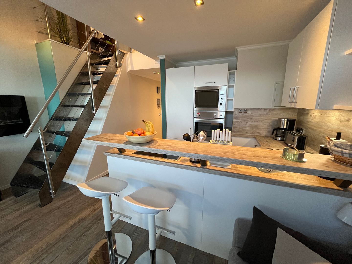A modern kitchen with a central island, bar stools, a built-in oven, and a staircase leading to an upper level.
