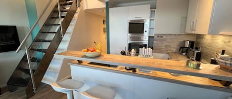 A modern kitchen with a central island, bar stools, a built-in oven, and a staircase leading to an upper level.