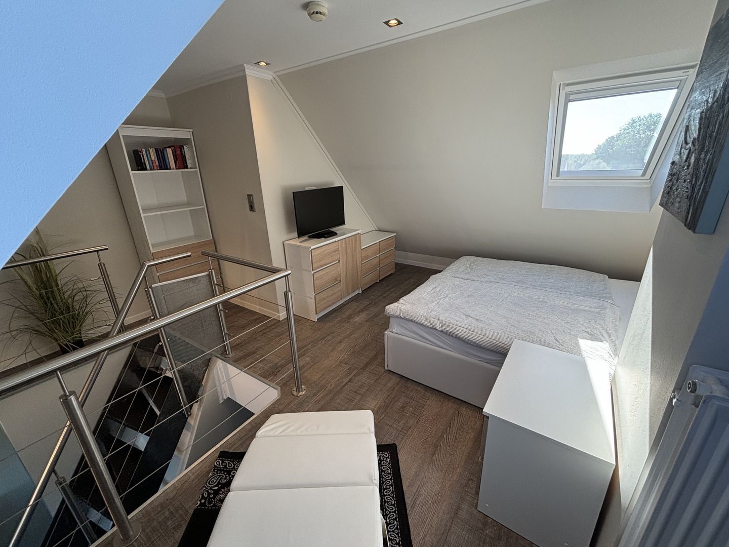 Ein modernes Schlafzimmer mit Bett, Fernseher, Bücherregal und einer Treppe.