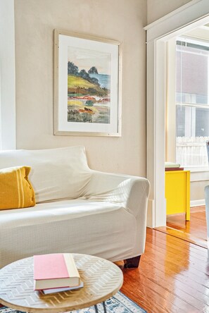 A room with a white sofa, a yellow side table, a framed painting on the wall, and a view of the outdoors. - Historical Townhouse on UT campus | Free Parking | Minutes to Downtown ❤️ (Austin)