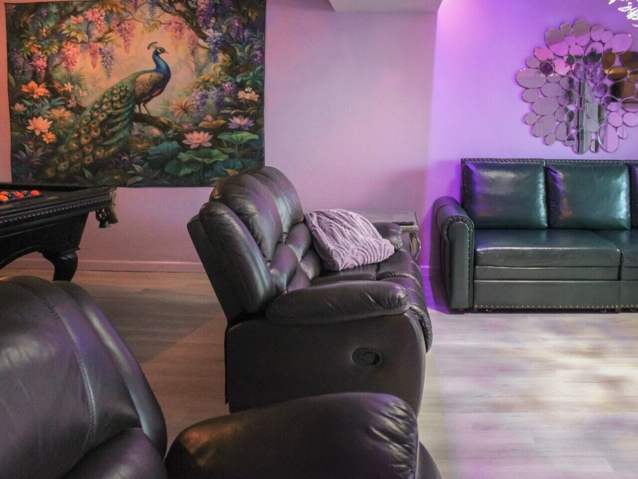 A room with a black leather sofa, a black armchair, a black piano, and a wall with a peacock painting.