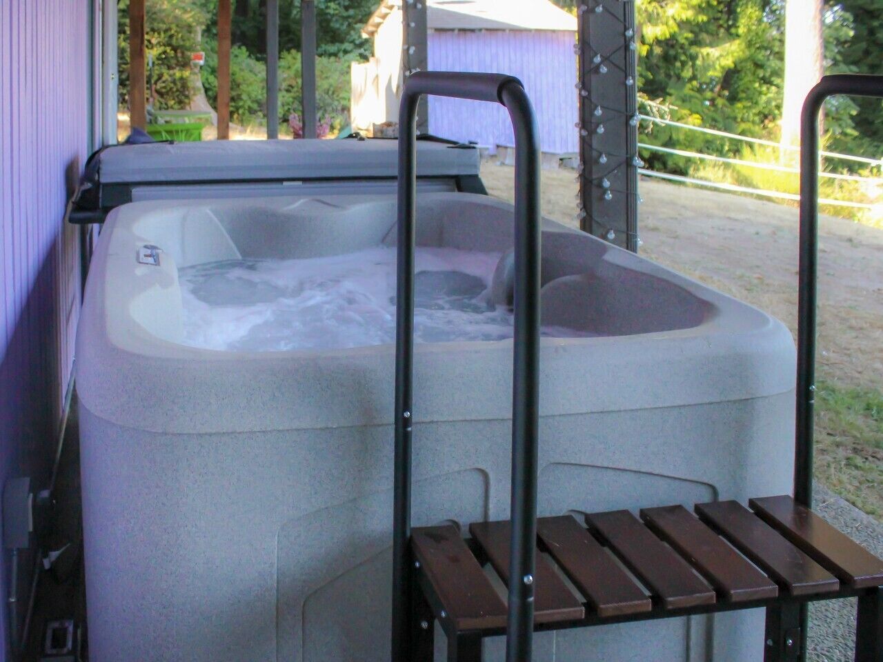 Ein Whirlpool mit Metallleiter und Holzstufen, umgeben von einem Zaun und Bäumen.