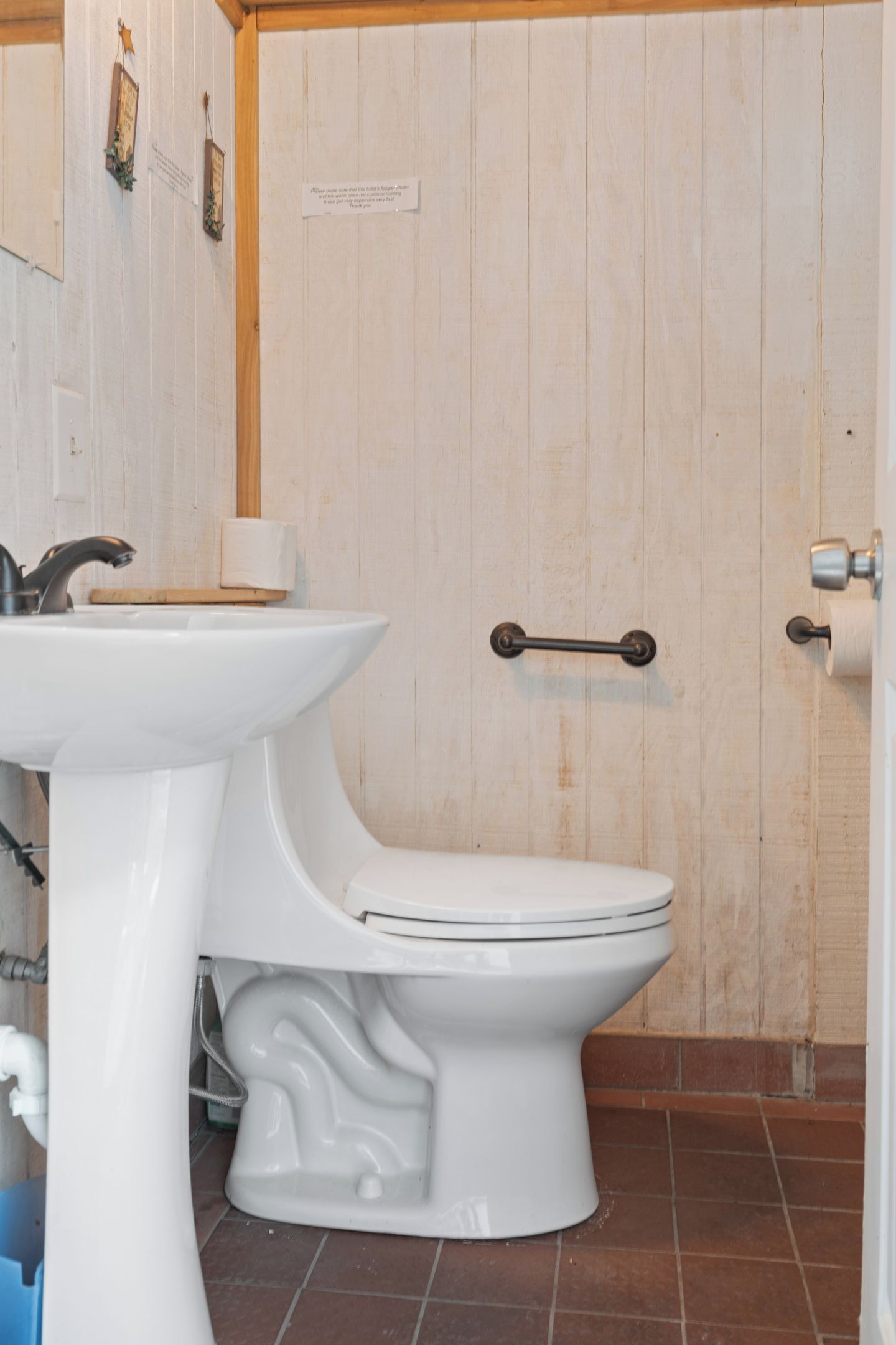 A bathroom with a white sink, a toilet, and a wooden door with a metal handle.