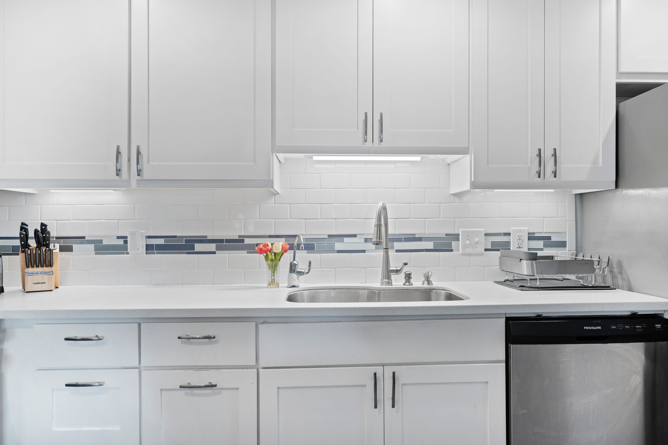 A modern kitchen with white cabinets, a stainless steel sink, and a dishwasher.