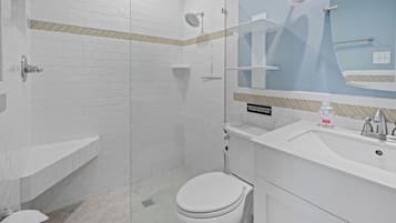 Ein modernes Badezimmer mit weißen Fliesen im U-Bahn-Stil, einer Glasdusche, einer Toilette, einem Waschbecken mit Spiegel und einem Schild, das darauf hinweist, keine Papierhandtücher oder Hygieneartikel auszuspülen.