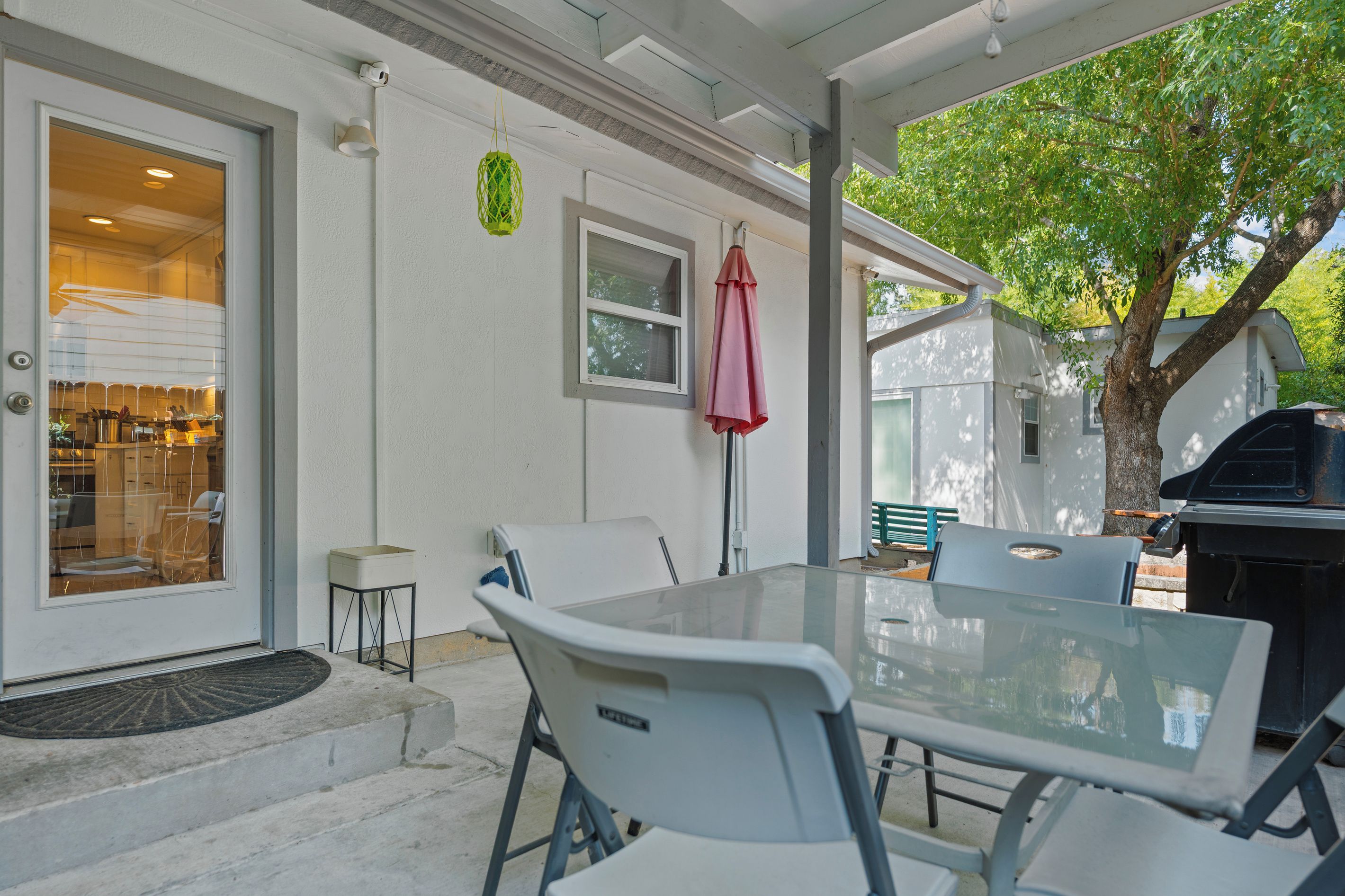 A covered patio with a glass table and chairs, a barbecue grill, and a door leading to a kitchen.