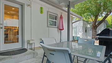 A covered patio with a glass table and chairs, a barbecue grill, and a door leading to a kitchen.
