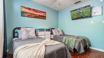 Ein Schlafzimmer mit zwei Betten, einem Deckenventilator, einem an der Wand befestigten Fernseher und Kunstwerken.