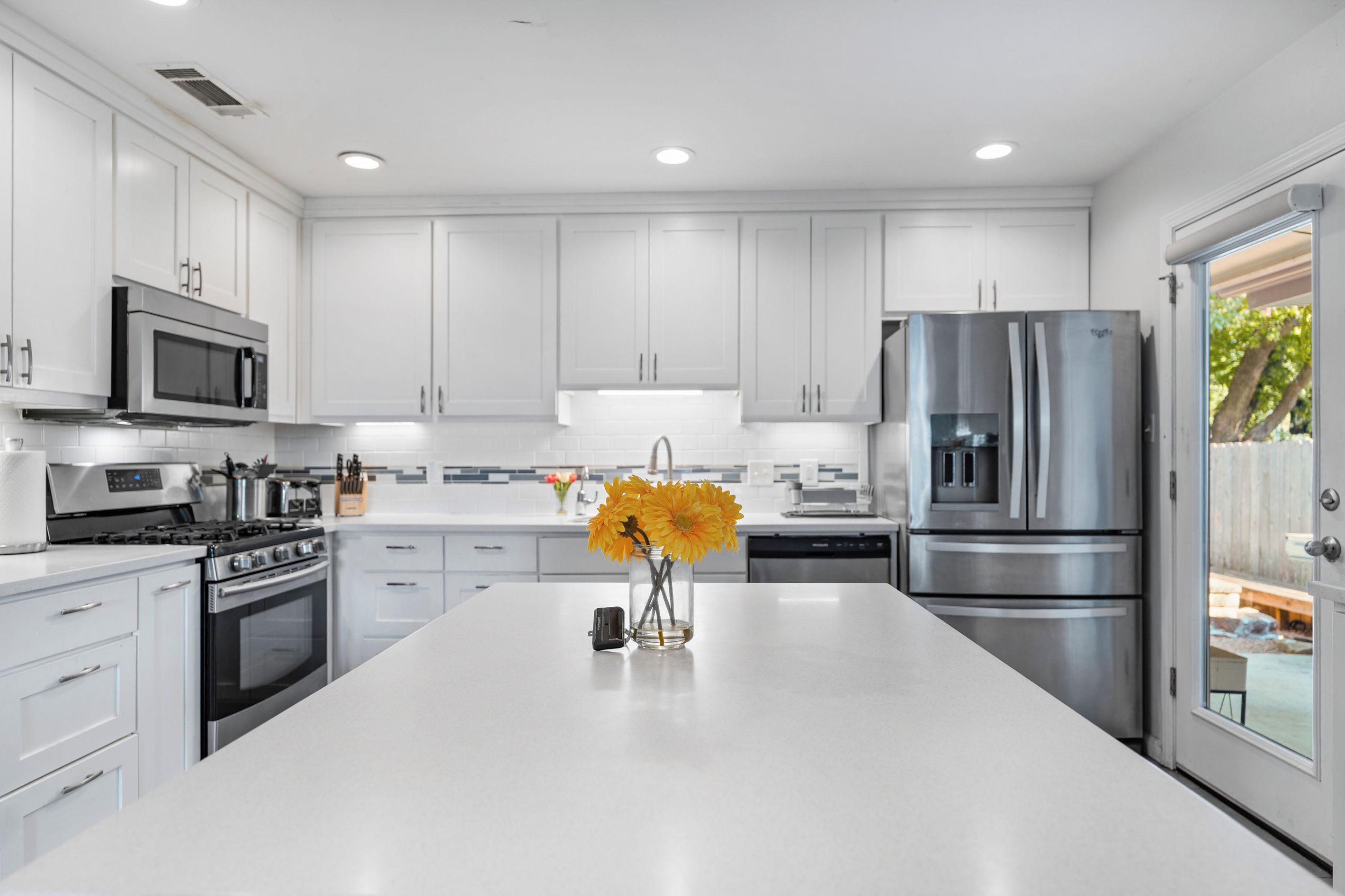 A modern kitchen with white cabinets, stainless steel appliances, and a central island with a vase of flowers.