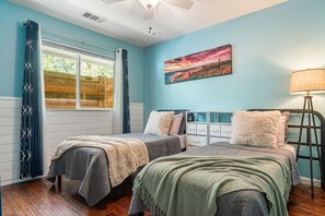 Une chambre avec deux lits, une fenêtre avec des rideaux, un tableau au mur et une lampe sur pied.
