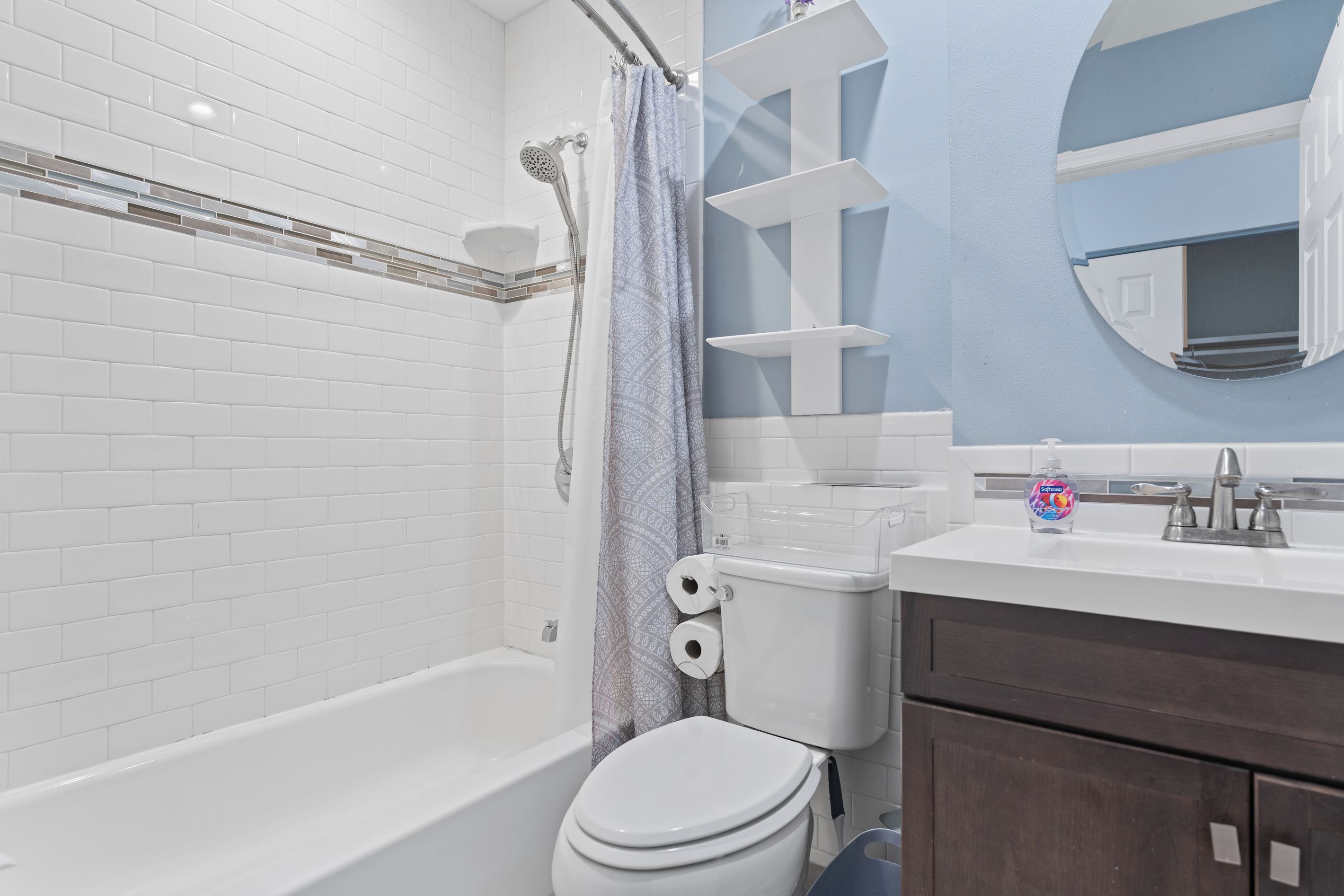 A bathroom with a white bathtub, a toilet, a shower, and a sink with a soap dispenser.