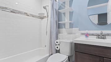 A bathroom with a white bathtub, a toilet, a shower, and a sink with a soap dispenser.