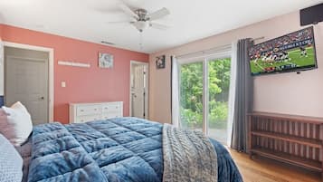 A bedroom with a bed, a ceiling fan, a TV mounted on the wall, and a sliding glass door leading to a balcony.