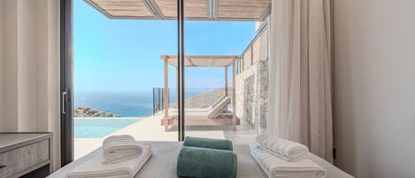 A bedroom with a large sliding glass door leading to a balcony with a view of the sea.