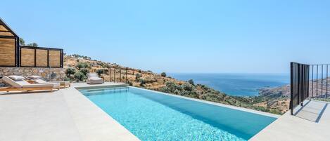 A swimming pool with a clear view of the sea and hills.