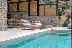 A poolside area with lounge chairs and a stone wall. - Metatulia Villa 7 – Private Pool, Jacuzzi & Views (Plakias)