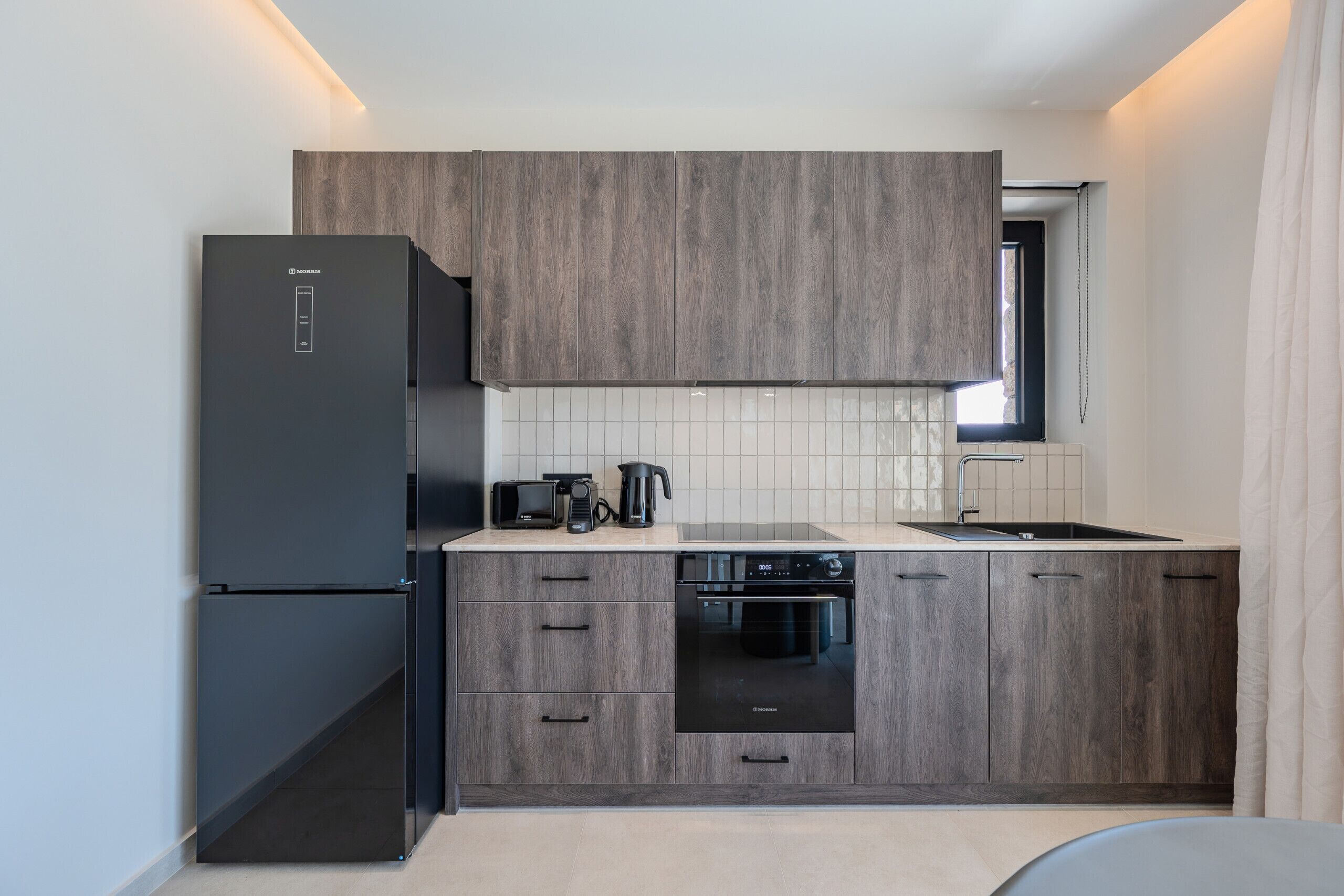 Cocina compacta con refrigerador, tostadora, cafetera, horno y ventana.
