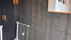 Et værelse med mørk træpanellering, en hvid radiator og et spejl der reflekterer en dør og billeder i rammer.