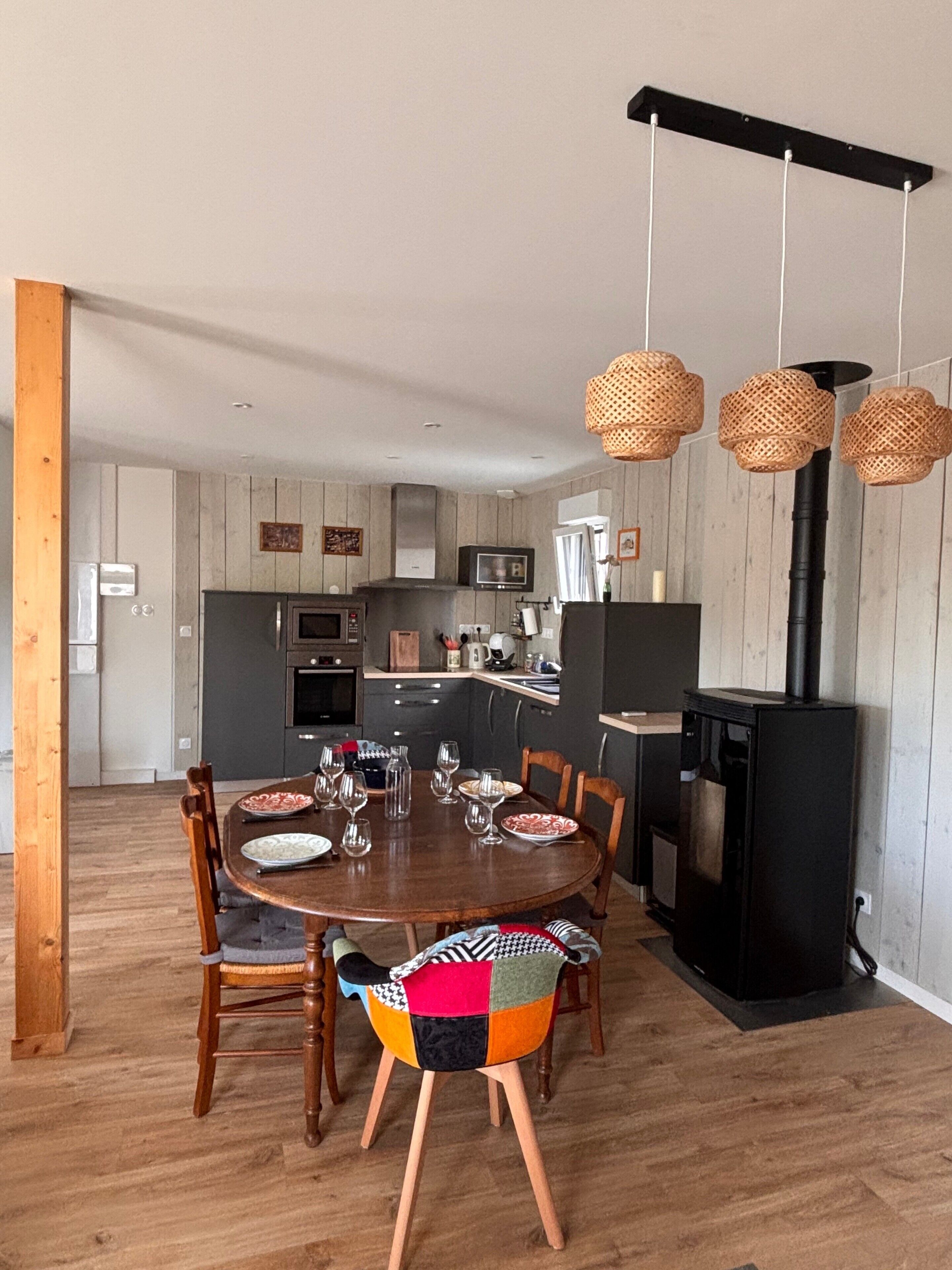 Une cuisine moderne avec un îlot central, des chaises en bois et des luminaires suspendus en rotin.