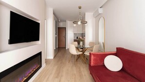 Una sala moderna con televisor de pantalla plana, chimenea, un sofá rojo y un comedor con mesa y sillas de vidrio.
