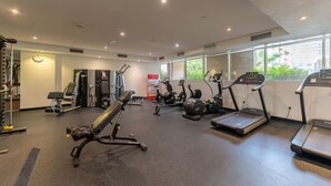Un gimnasio con diversos equipos de ejercicio, incluyendo cintas de correr y máquinas de pesas, y amplias ventanas que dejan entrar luz natural.
