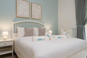 A neatly made bed with white bedding and pillows, a bedside table with a lamp, and two framed floral wall art pieces. - The Belgravia Residence | Refined 1BR in JVC (Jumeirah Village Circle (JVC))