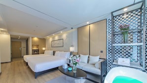 Una habitación de hotel moderna con una cama grande, un sofá, una mesita y una bañera.