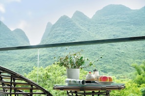A table with a potted plant, teapot, teacup, and peaches, set against a mountainous backdrop. - Liangsu Shili Jiangshan Hotel (Guilin)