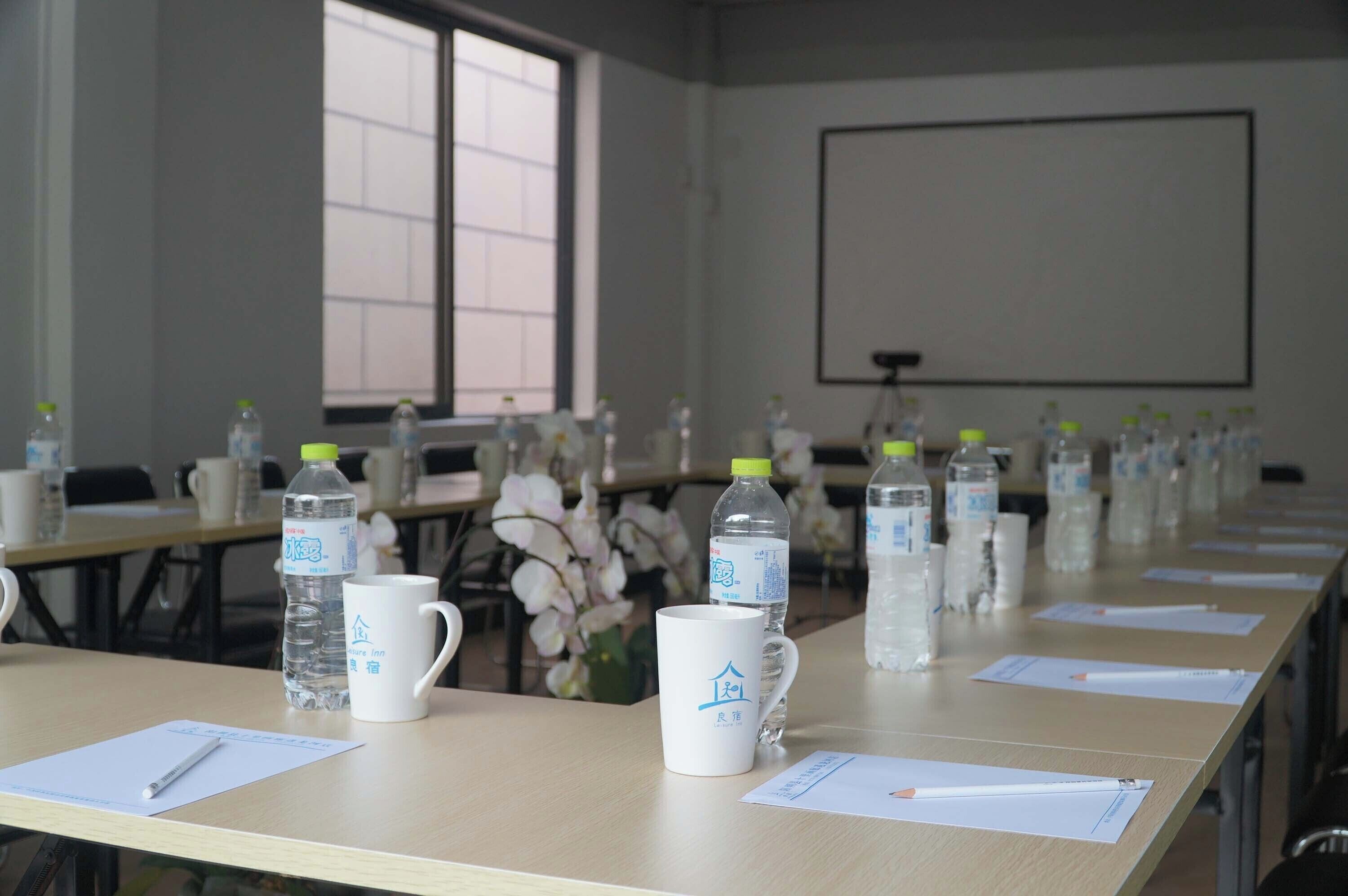 Un salón de conferencias con mesas dispuestas para una reunión, cada una con una botella de agua, una taza y papeles.