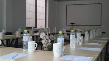 Un salón de conferencias con mesas dispuestas para una reunión, cada una con una botella de agua, una taza y papeles.