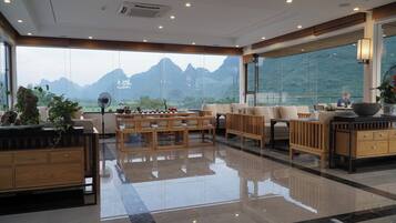 A spacious living area with a view of mountains through large windows, wooden furniture, and a polished floor.