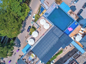 An aerial view of a building with a swimming pool, multiple cars parked in front, and a large tree to the left. - Liangsu Shili Jiangshan Hotel (Guilin)