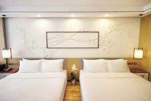Una habitació d'hotel amb dos llits, una obra penjada a la pared, làmpades de nit i una petita planta en test.