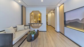 Interior moderno com sofá, mesa de centro com planta, corredor que leva a um quarto e uma pintura na parede.