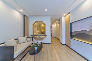 A modern interior with a sofa, a coffee table with a plant, a hallway leading to a bedroom, and a painting on the wall. - Liangsu Shili Jiangshan Hotel (Guilin)