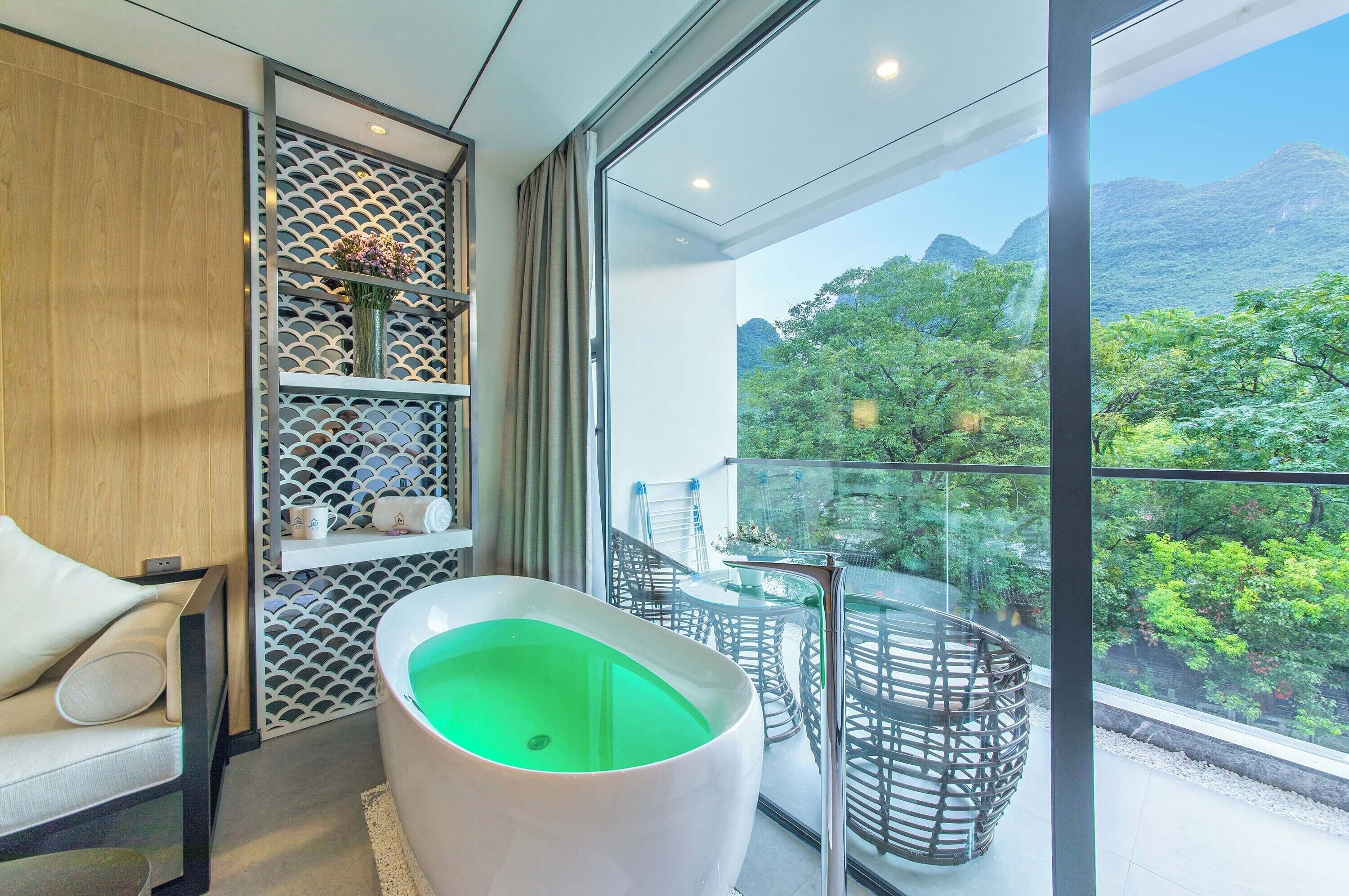 A modern bathroom with a large bathtub, a glass-enclosed balcony with a view of lush greenery and mountains.