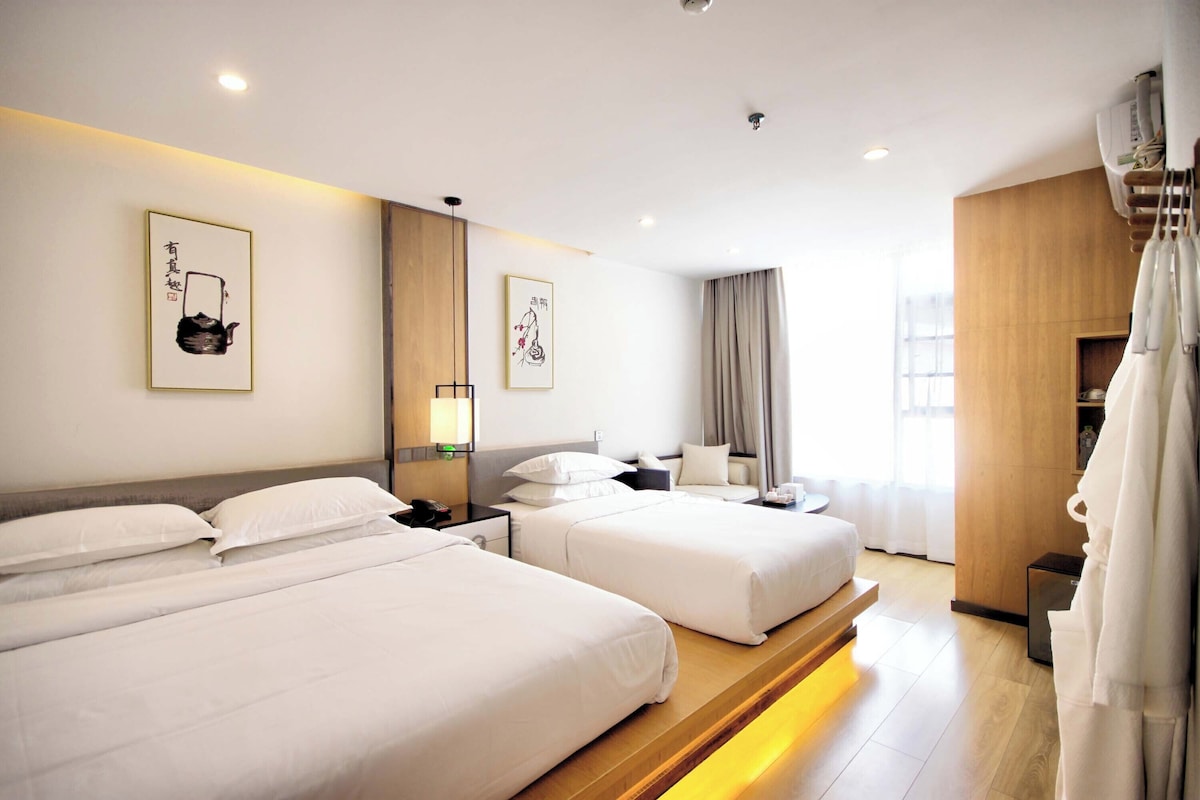 A hotel room with two beds, a desk, a chair, a wardrobe, and artwork on the walls.