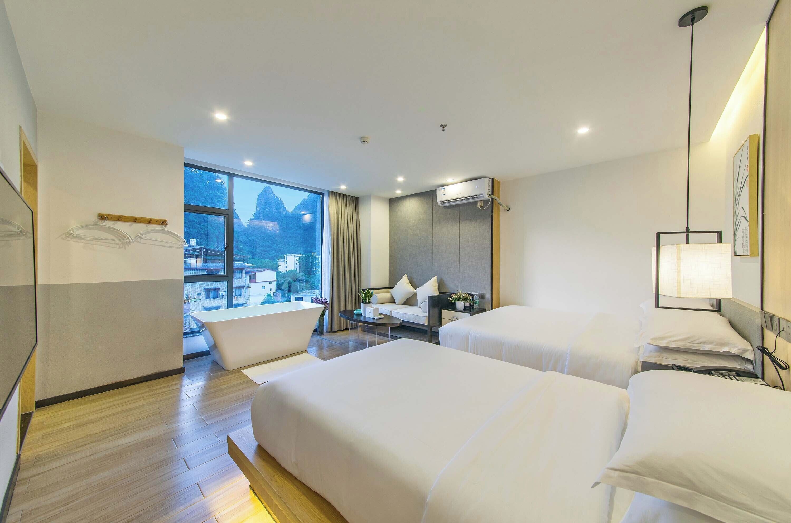 A hotel room with two beds, a sitting area, a large window with a view, and an air conditioning unit.