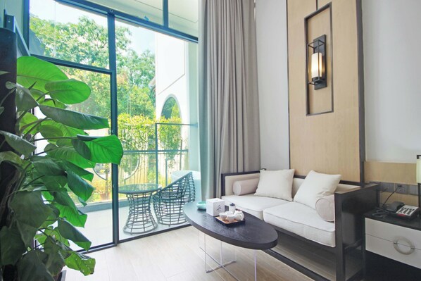 A modern hotel room with a balcony, a sofa, a small table, and a potted plant.