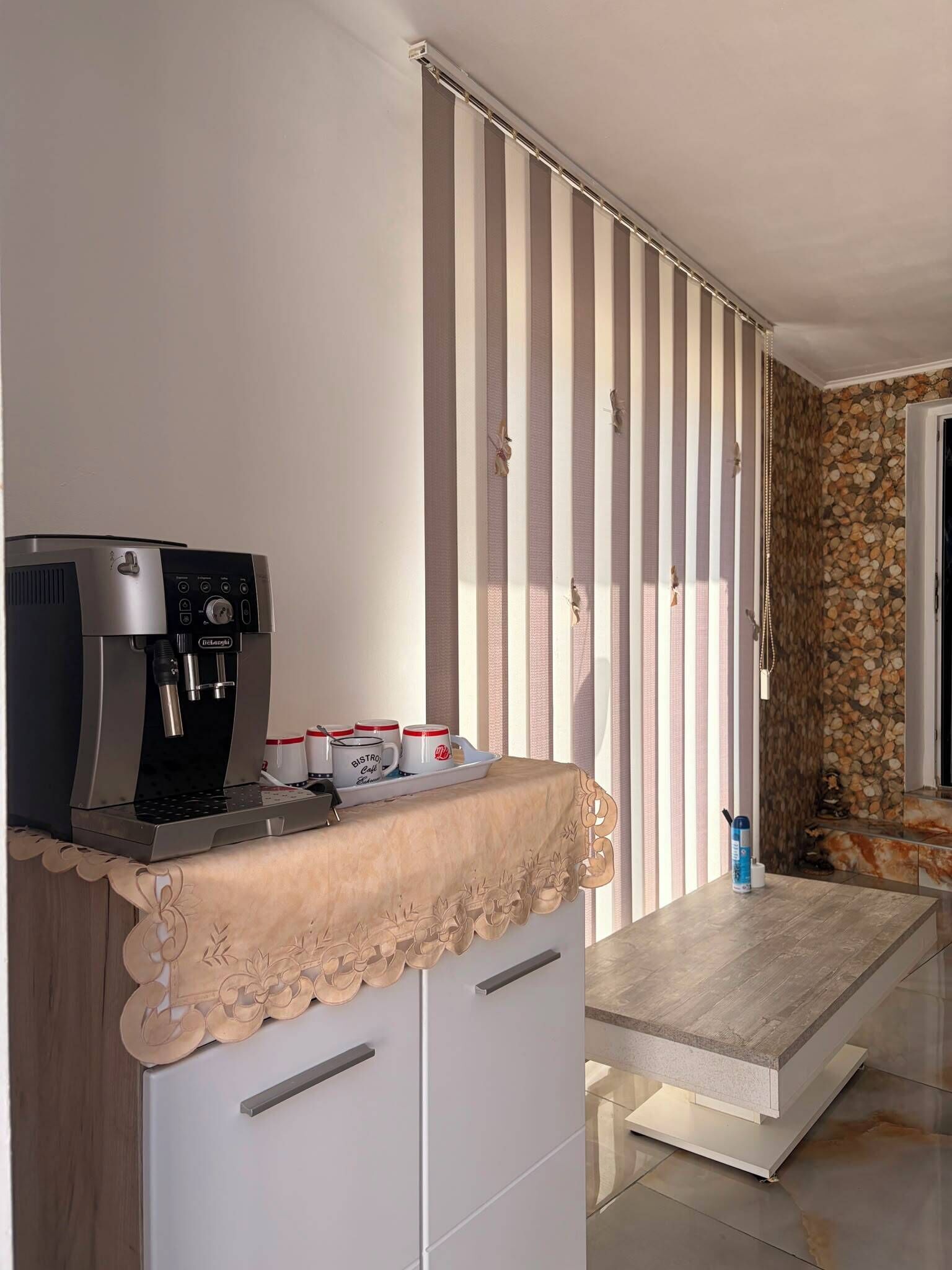 Une petite cuisine équipée d’une machine à café, une petite table avec une nappe et un rideau à rayures.