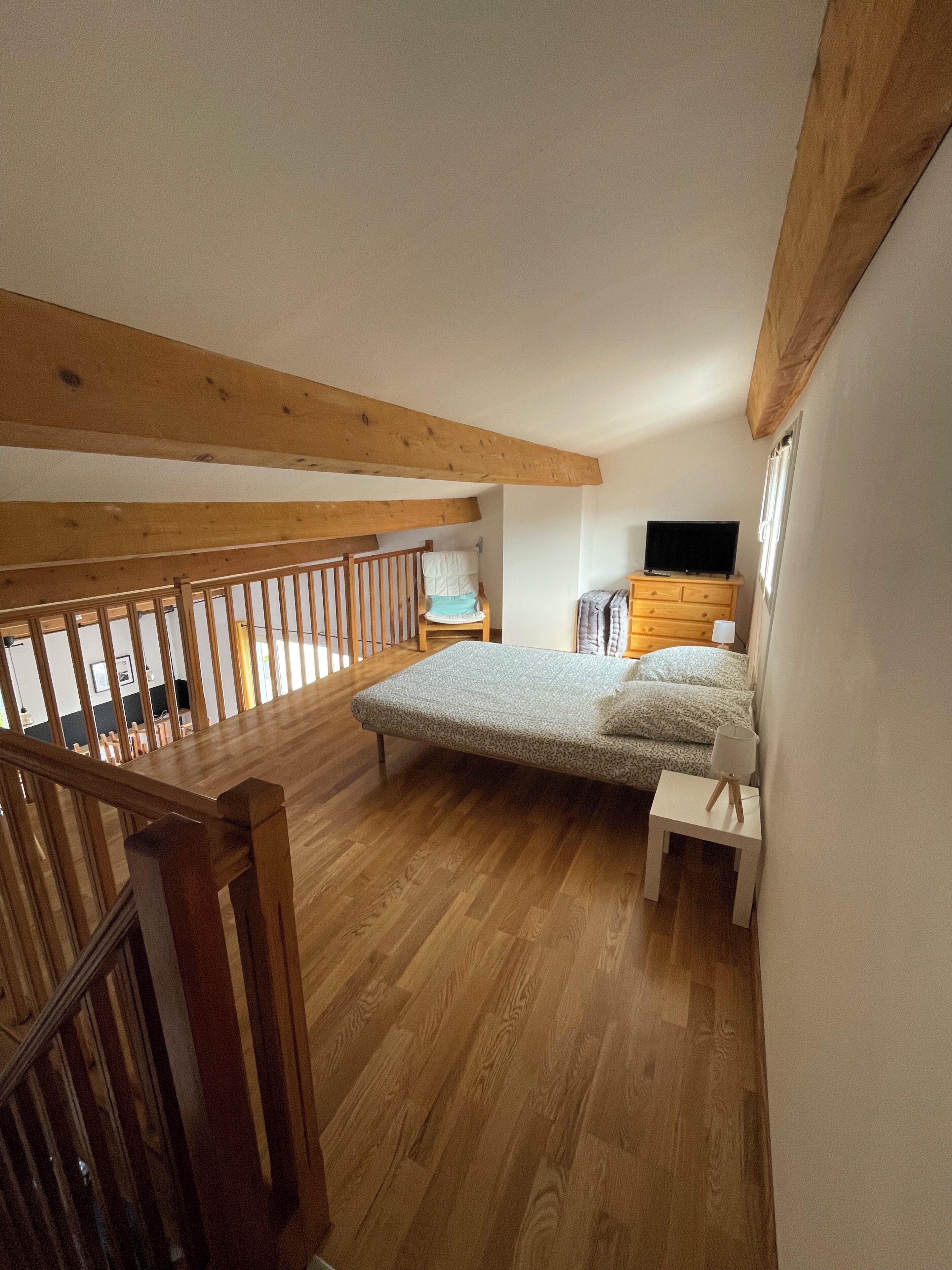 A bedroom with a wooden floor, a bed, a TV, a dresser, and a window.