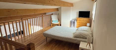 A bedroom with a wooden floor, a bed, a TV, a dresser, and a window.