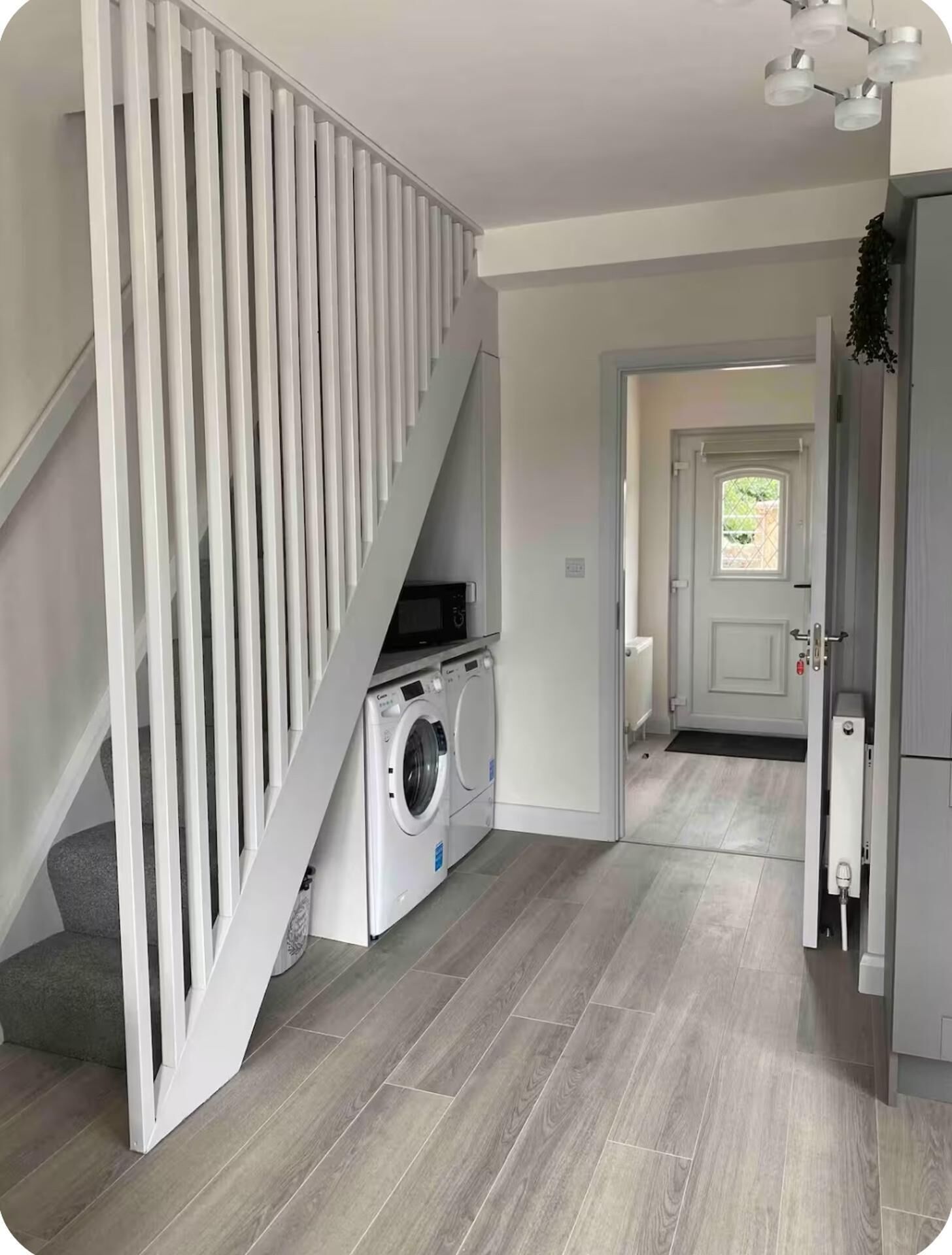 A laundry area with a washing machine and dryer, a staircase with white railings, and a door leading to another room.