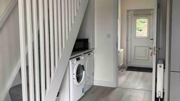A laundry area with a washing machine and dryer, a staircase with white railings, and a door leading to another room.