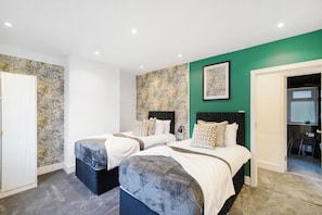 A bedroom with two beds, a green accent wall, and a framed artwork above the beds. - Charming 3-bedroom house in welcoming London neighborhood (london)